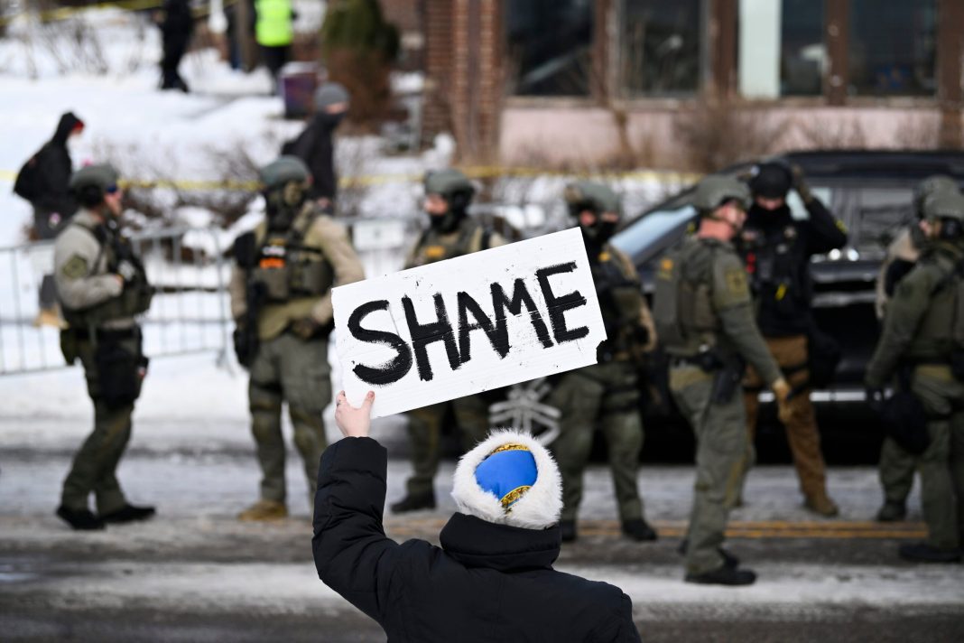 An onlooker holds a sign that reads "Shame" as members of law enforcement work the scene following a suspected shooting by an ICE agent during federal law enforcement operations on January 07, 2026 in Minneapolis, Minnesota. 