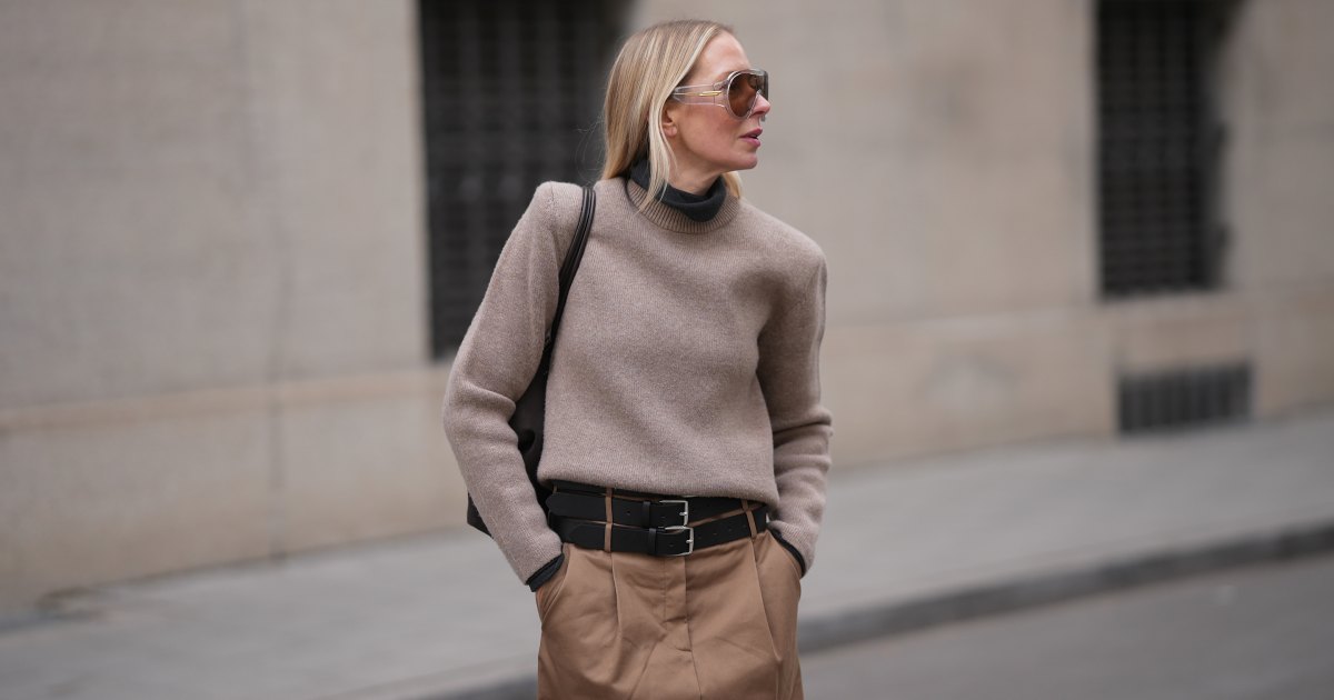 MUNICH, GERMANY - JANUARY 22: Mirja Klein is seen wearing a dark grey turtleneck sweater with slim fit from The Frankie Shop; a beige sweater with padded shoulders, crew neck and long sleeves layered over from COS; a light brown midi skirt with pleated front pockets, A-line silhouette and three black layered leather belts with silver buckles from MeiMeij; oversized shield sunglasses with transparent acetate frame and brown tinted lenses from Bottega Veneta; a dark chocolate brown suede leather shoulder bag with smooth leather top handles called 