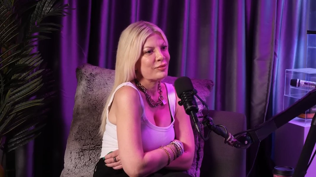 Tori Spelling crosses her arms under beautiful purple lighting in 2025.